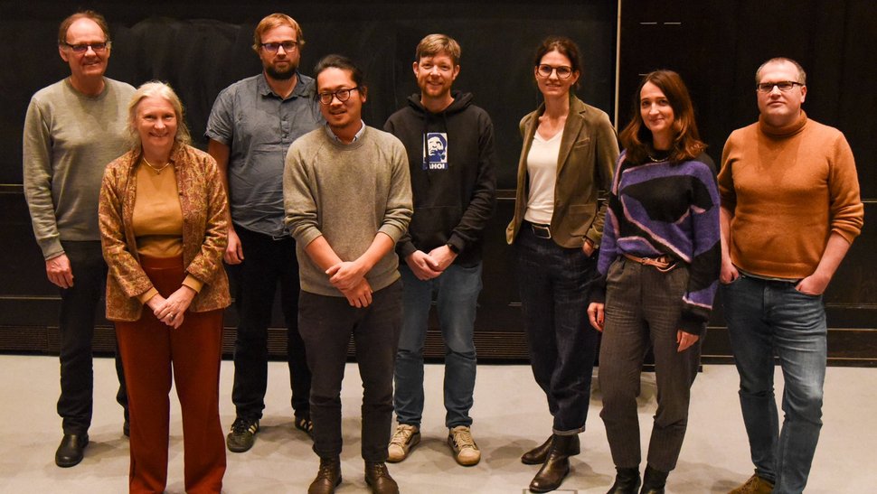 Das Foto zeigt zehn Forscherinnen und Forscher vor einer Leinwand im Hörsaal stehen.