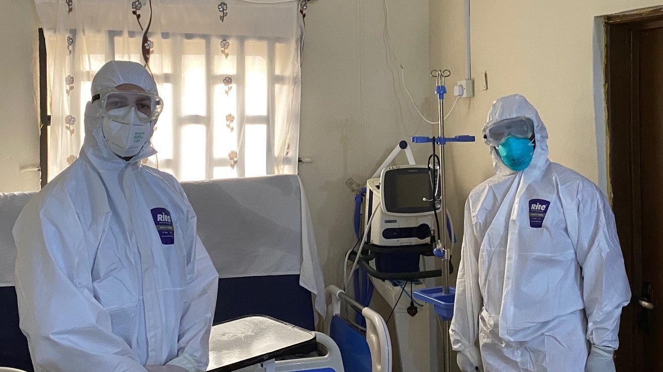 The photo shows two people in personal protective suit standing in a ward.