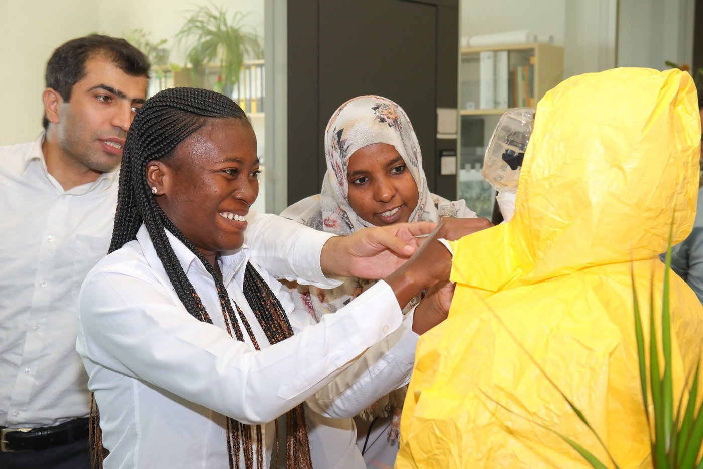 The photo shows three diverse people helping a fourth to put on a personal protective suit.