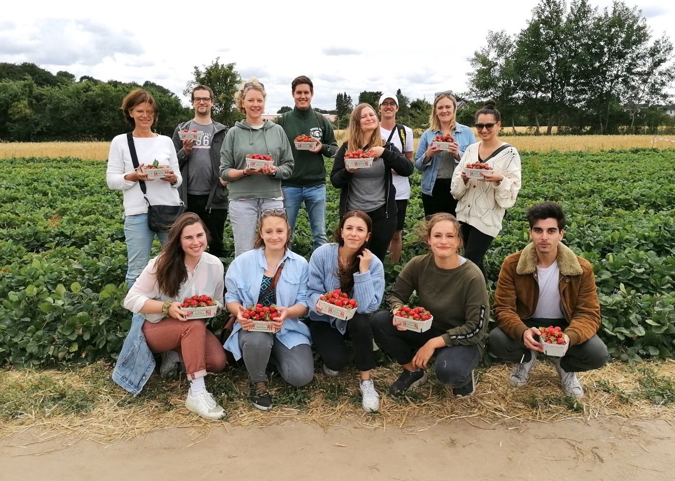 Betriebsausflug der AG Molekulare Infektionsimmunologie: eine Gruppe steht vor einem Erdbeerfeld und halten jeweils eine Schale Erdbeeren in die Kamera.