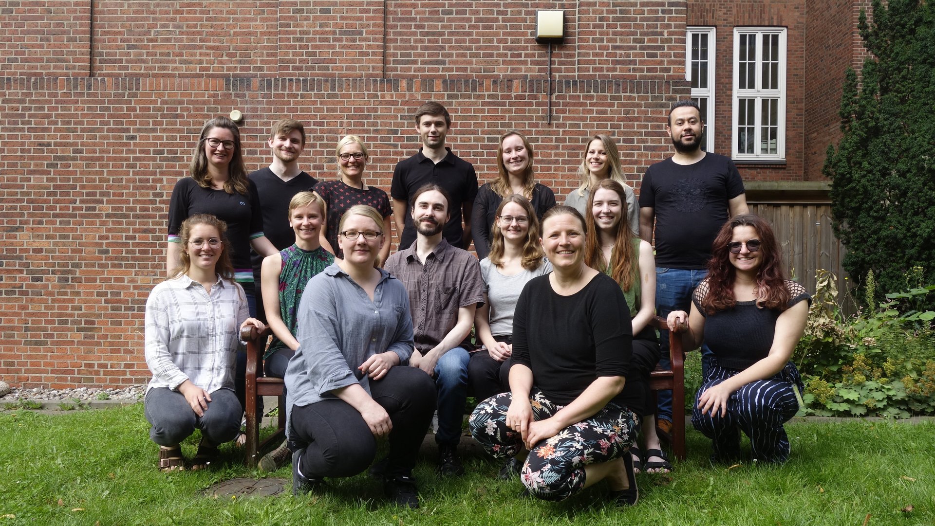 Members of the Leibniz Junior Research Group Oestereich are depicted here. Some are standing, others are sitting on a bench or kneeling in front of the bench, all with smiling faces.