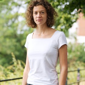 Dr Nathalie Vielle: a smiling researcher with curly hair in a white T-shirt on a sunny path under trees