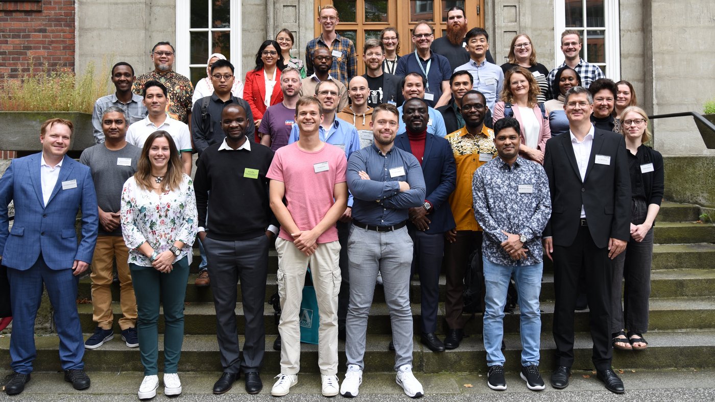 The picture shows a group of people standing in front of a building, all looking friendly into the camera.