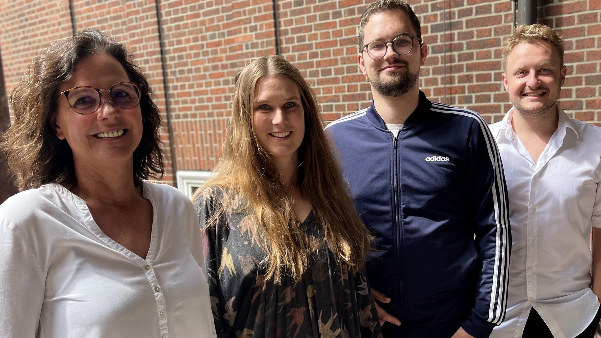 Bachmann laboratory group: a group of young researchers stands in front of the institute and laughs friendly into the camera.