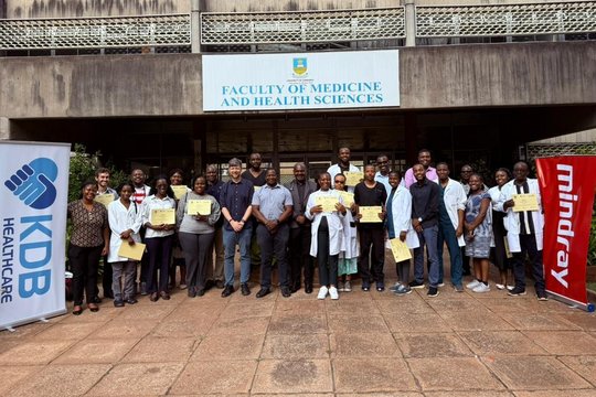 The picture shows a big group of people standing in front of a hospital. Some people have certificates in their hands.