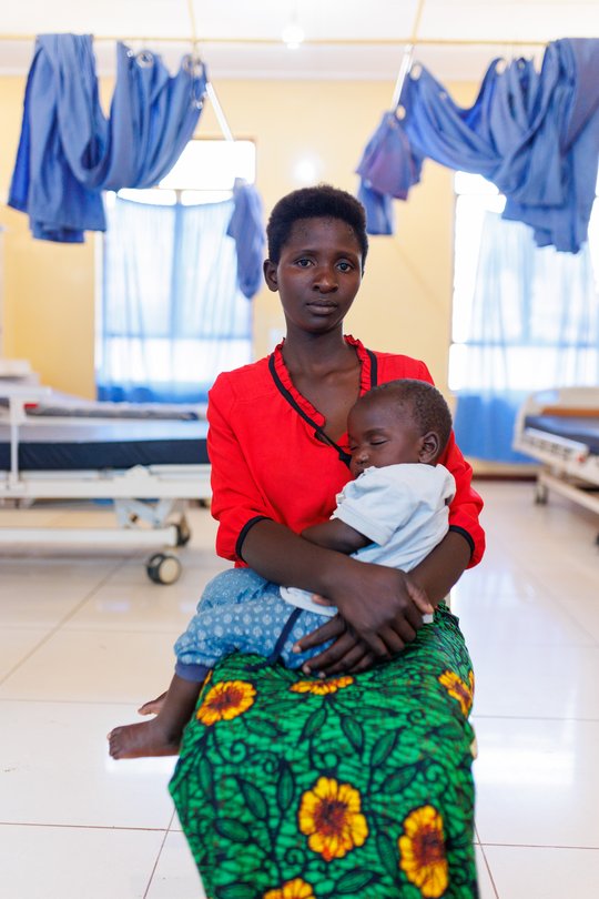 Das Bild zeigt eine malawische NTD-Überlebende der Schlafkrankheit mit ihrem Kind auf dem Schoß.