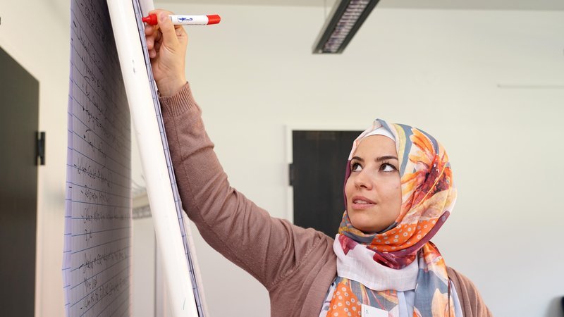 Eine Wissenschaftlerin mit einem Kopftuch schreibt konzentriert Notizen an ein Flipchart.