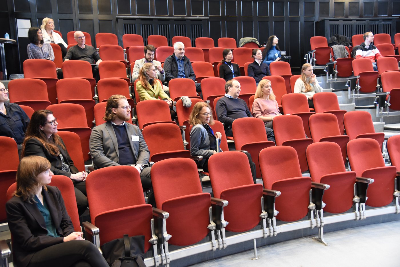 Im historischen Hörsaal Das Bild zeigt das Publikum im historischen Hörsaal auf rot gepolsterten Klappsitzen vor dunel getäfelten Holzwänden.