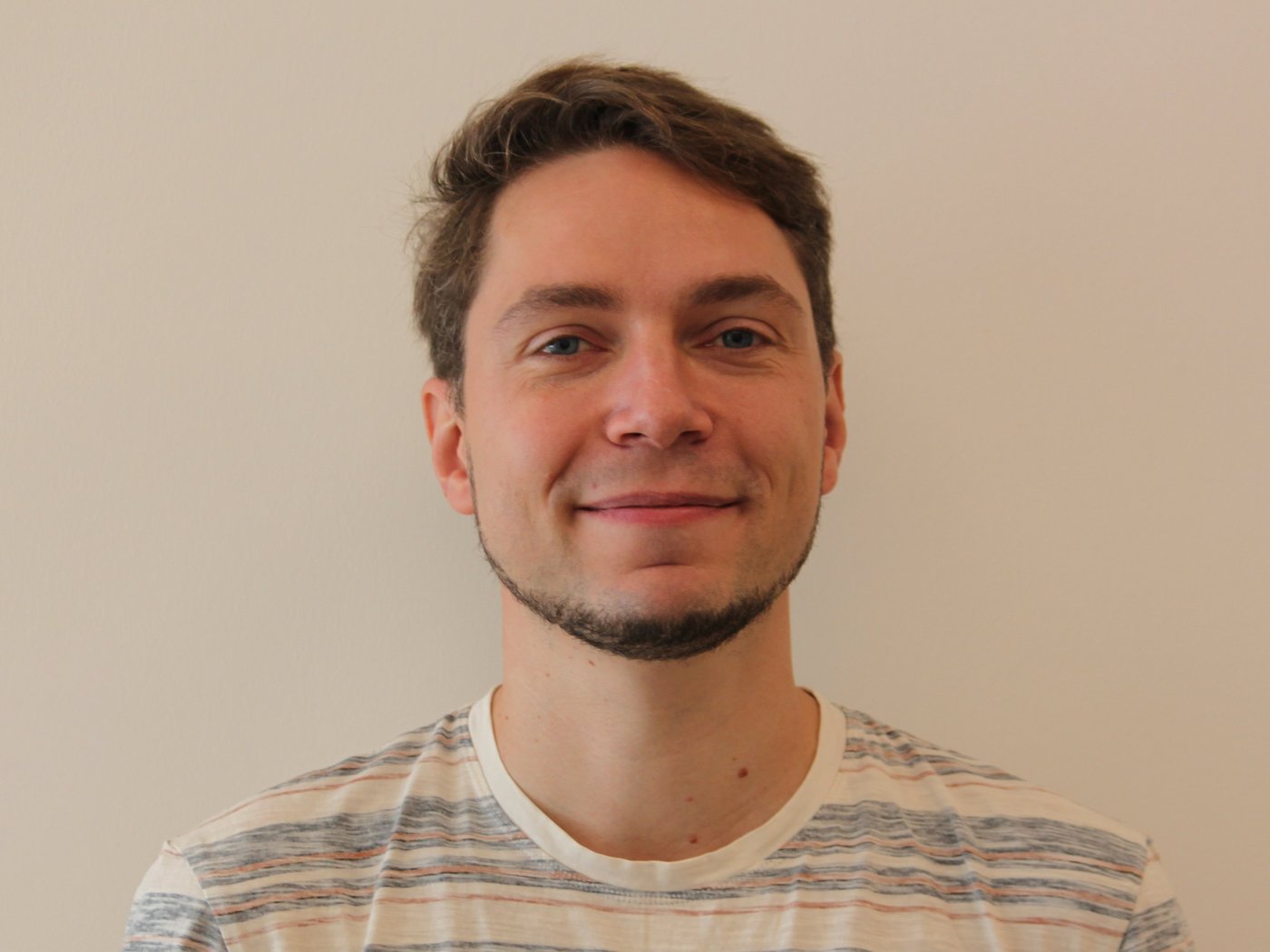 Dr. Joachim Matz: ein Forscher, der in die Kamera lächelt. Er trägt ein gestreiftes Shirt, einen Bart an Kinn und Hals und kurzes braunes Haar.