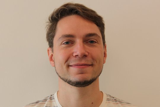 Dr. Joachim Matz: ein Forscher, der in die Kamera lächelt. Er trägt ein gestreiftes Shirt, einen Bart an Kinn und Hals und kurzes braunes Haar.