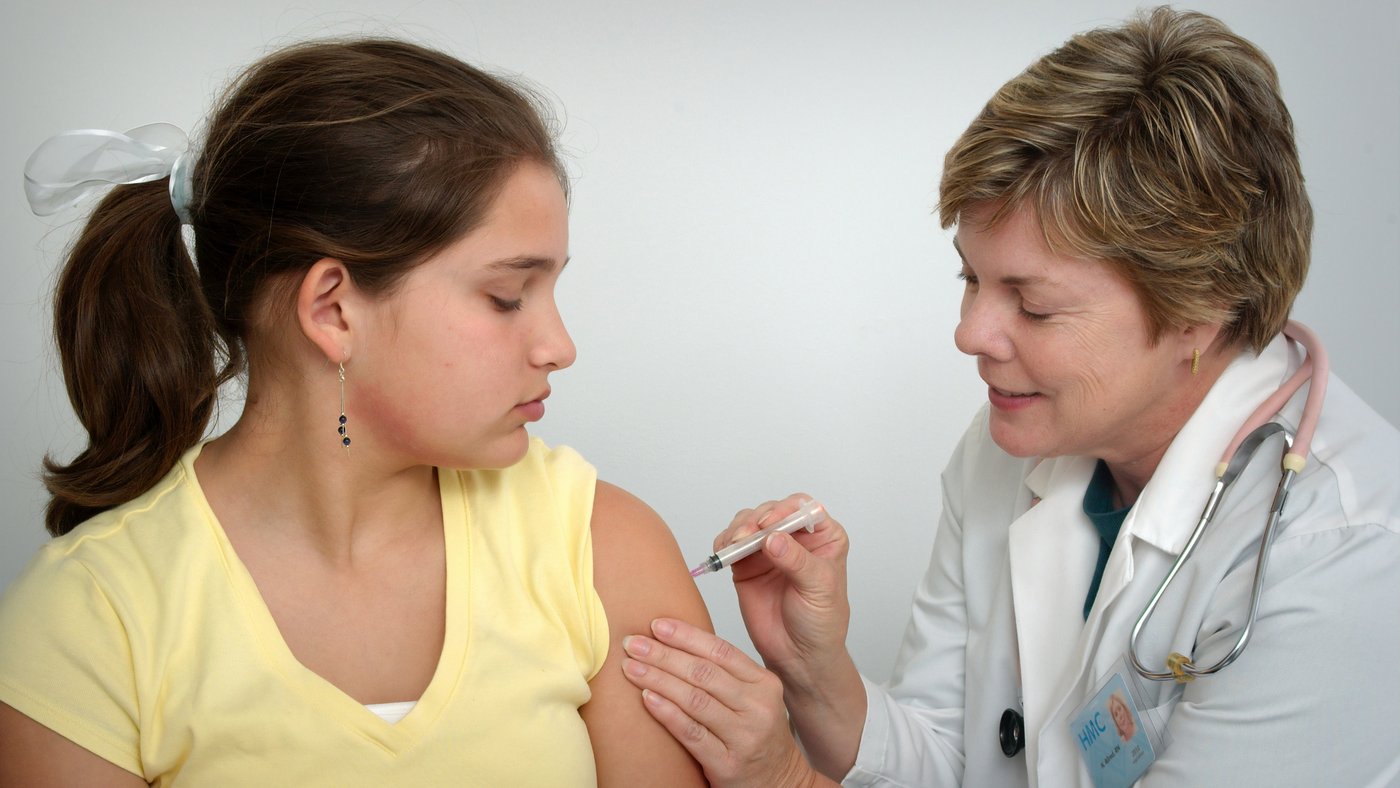Eine Person wird von einer Ärztin in weißem Kittel mit einer Spritze in den Oberarm geimpft.