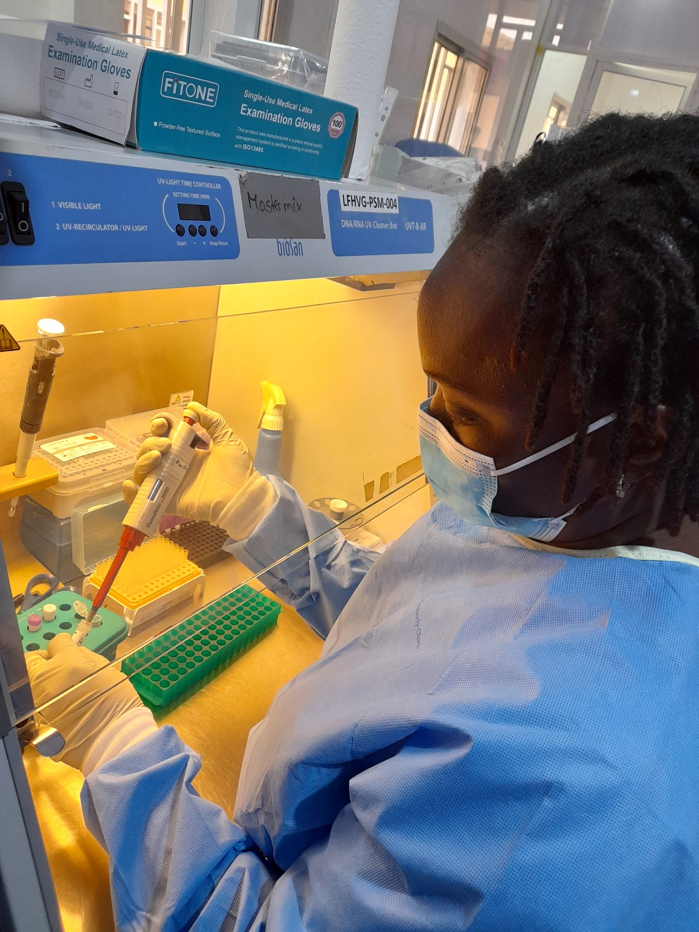 Lab staff preparing real time PCR mastermix for mpox detection during hands-on training at CRV-LFHVG. October 2024, Conakry, Guinea one laboratory staff pipetting from a tube under a cabinet wearing bright blue PPE.