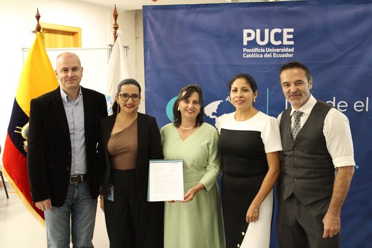 Institutionenübergreifendes Team Gruppenfoto vor ecuadorianischer Fahne und PUCE-Banner