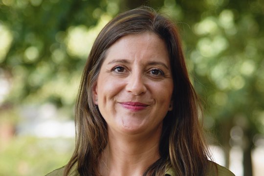Dr. Sophie Duraffour: eine Frau mit grüner Bluse und schwarzer Hose auf einem sonnigen Weg mit Bäumen im Hintergrund. Sie hat dunkle, lange Haare.