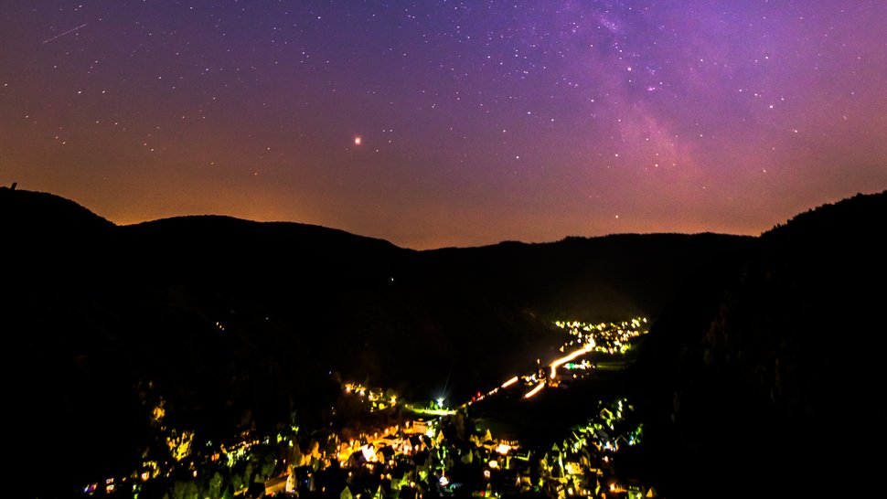 Lichtverschmutzung Das Foto zeigt einen städtischen Nachthimmel mit starker Lichtverschmutzung über den umgebenden Bergen.
