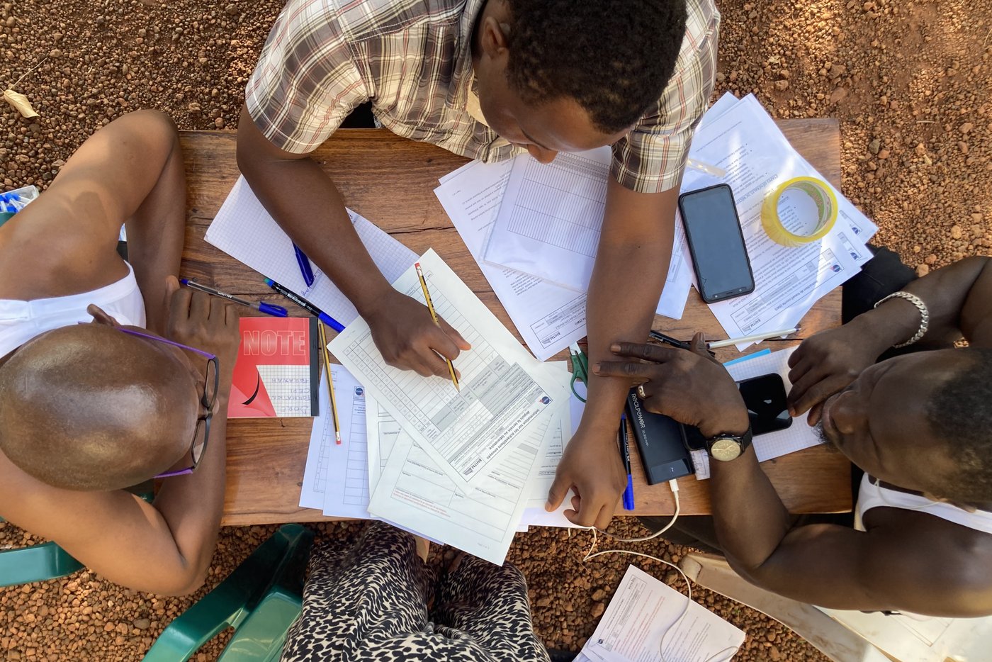 Completing study documentation in the field. Four scientific study staff sitting around a table outside; one of the staff is filling in a form.