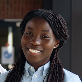 Jennifer Antwi-Ekwuruke: eine Doktorandin lächelt in die Kamera. Sie trägt lange schwarzes Haare, die zu kleinen Zöpfen geflochten sind und eine blaue Bluse.