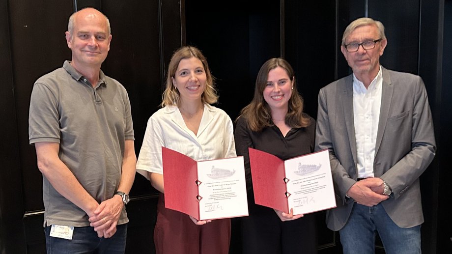 Group photo: two older gentlemen on the outside, the two young female scientists inside with certificates in their hands