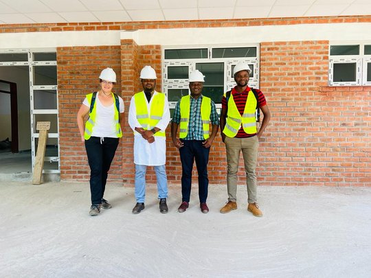 The picture shows four people wearing high-visibility vests and safety helmets in front of a building. They are all smiling at the camera.