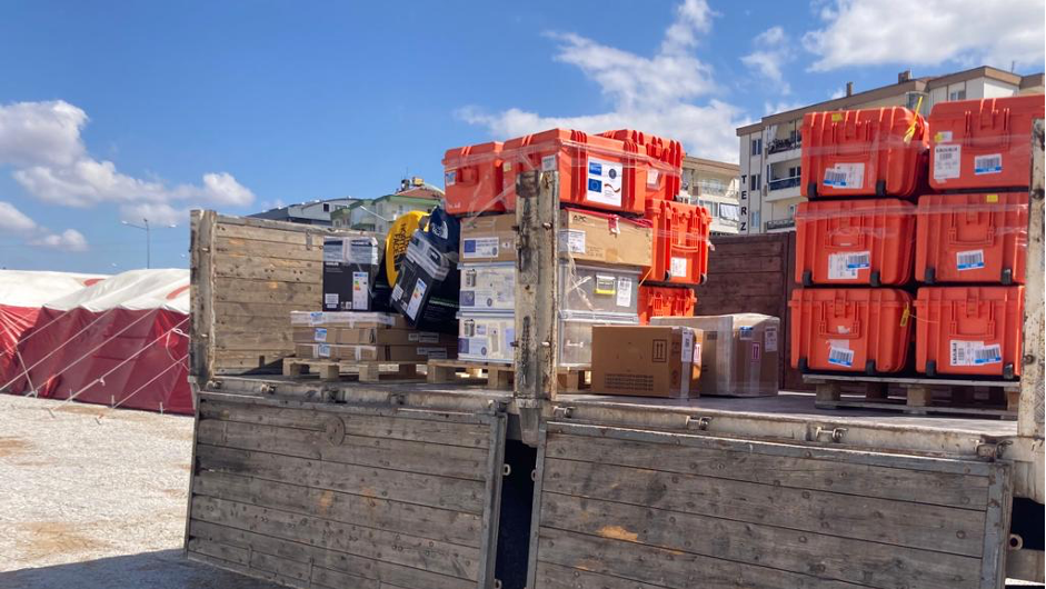 EMLab boxes arrive at the base in Çanakkale, Turkey, on a truck. The image shows a large truck with opened trailer that is loaded with stacks of orange transport boxes.