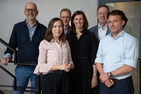 The Board of Trustees Photo of several middle-aged men and women in a modern exposed-concrete stairwell. They are smiling at the camera.