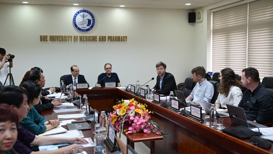 Das Bild zeigt mehrere Personen um einen Tisch mit Mikrofonen.