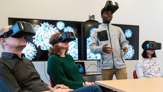 Several people with VR glasses. A man speaks into the round with pushed up glasses