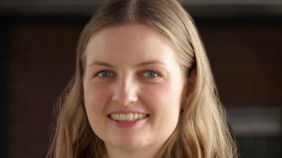 The picture shows a young female researcher in a light-coloured jumper, looking friendly at the viewer.