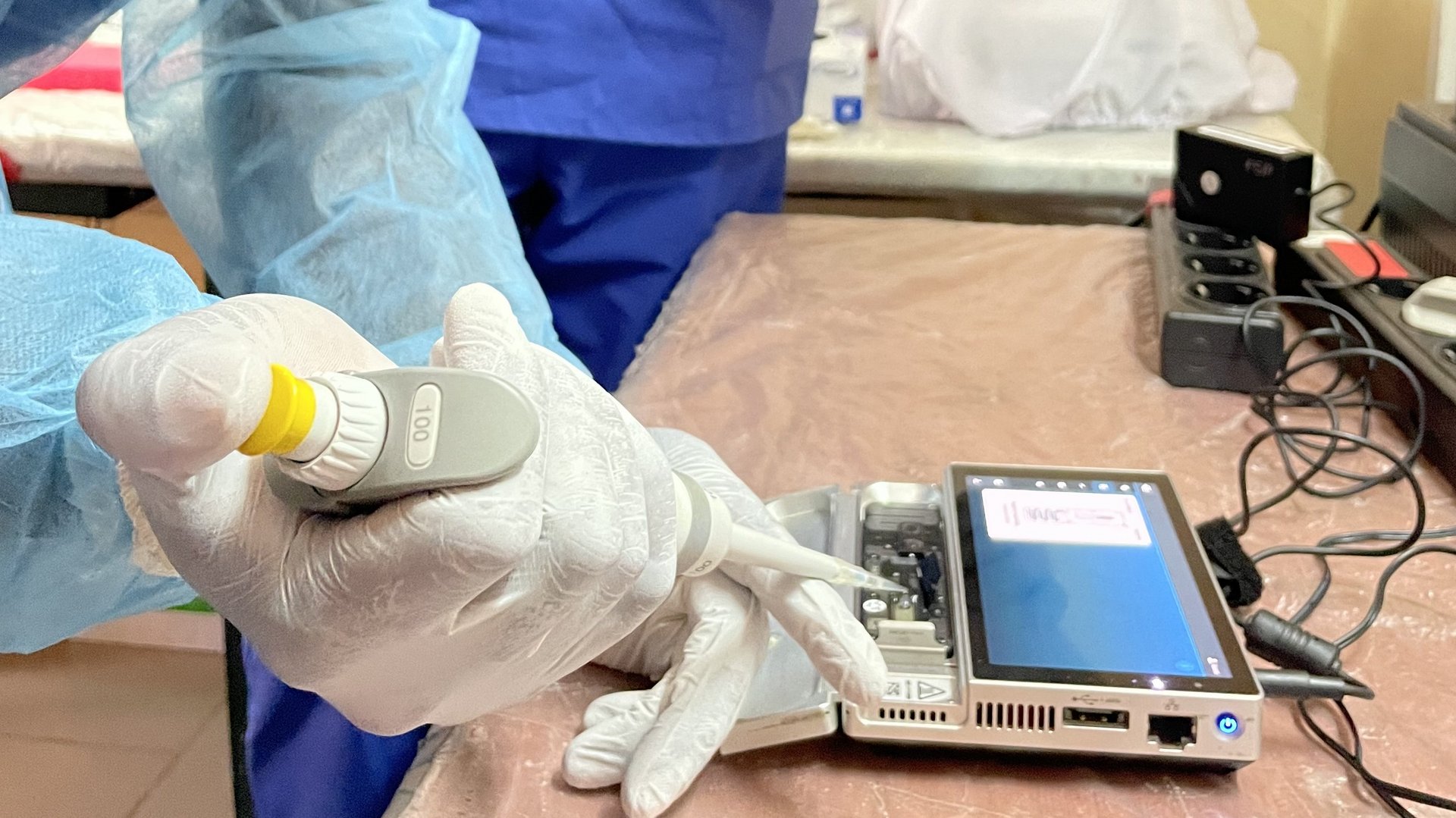 A scientific staff wearing personal protective gear using a pipette to load a sample into a sequencing device.