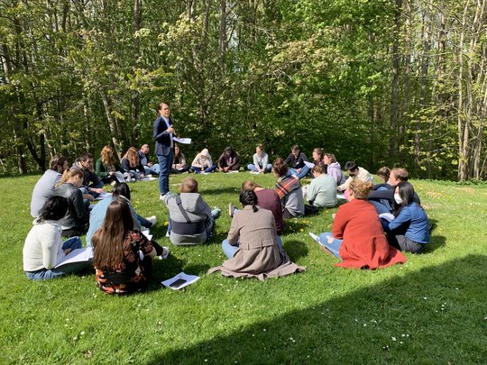 A scientist stands on the lawn in a circle of other participants of the LCI Summer School and gives a lecture.