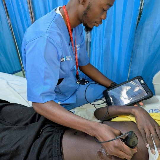 The picture shows a man scanning a patient with an ultrasound probe. At the same time he is looking at the ultrasound on a tablet.