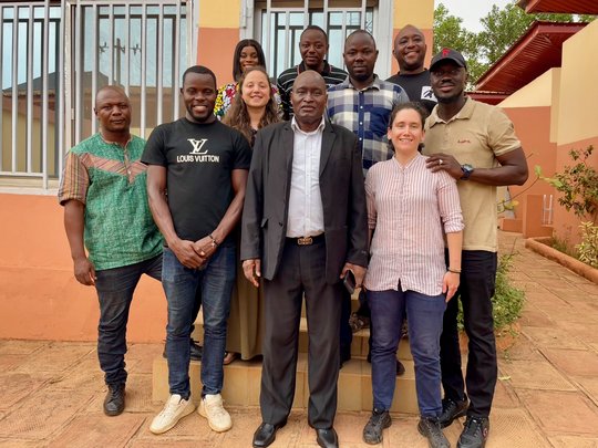Vor einem Gebäude versammeln sich mehrere Personen, posieren gemeinsam und wirken freundlich und zugänglich.