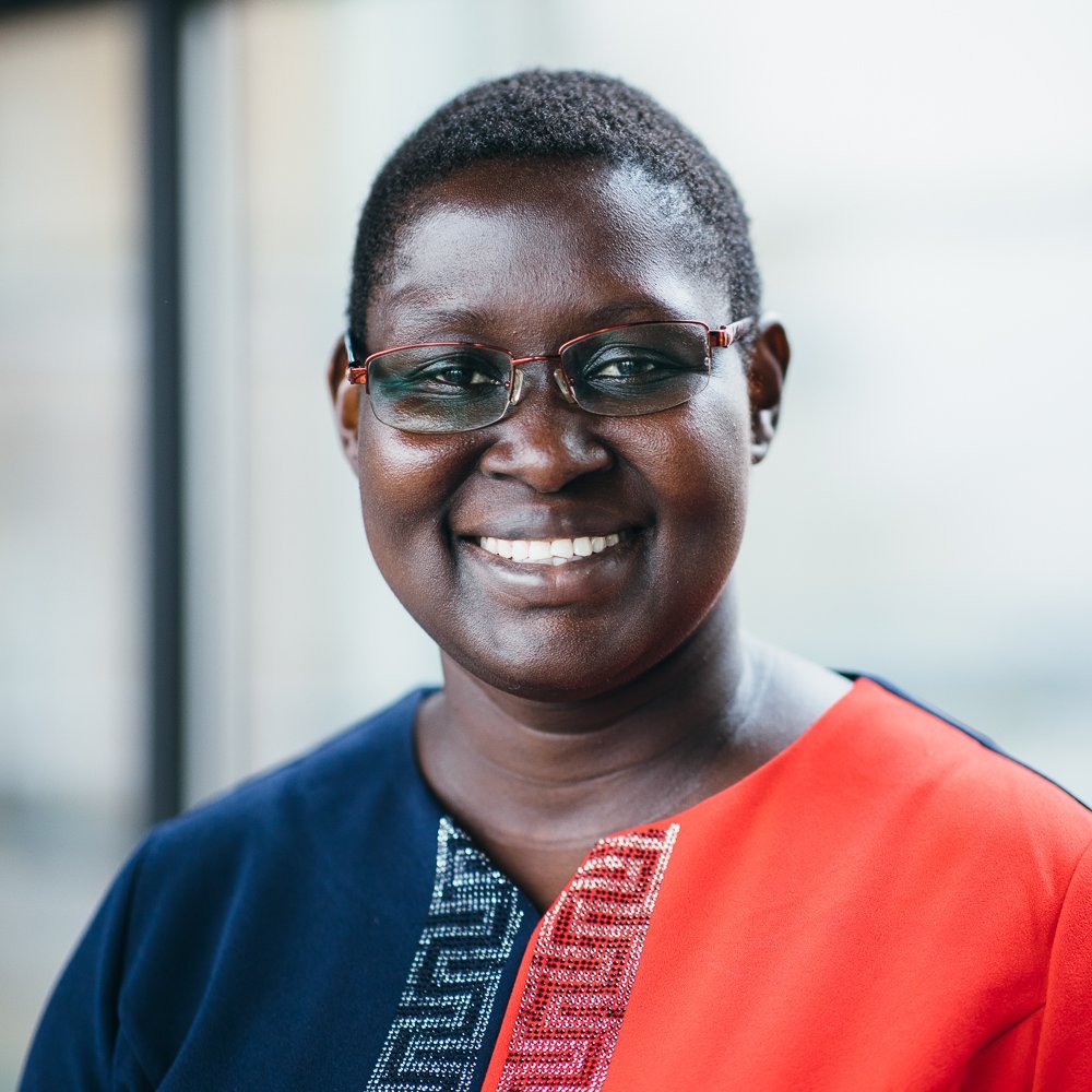 Portrait of a Black female person with glasses, wearing a blue and red dress.