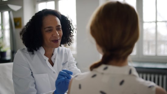 A doctor advises a patient, whom we look over her shoulder from behind.