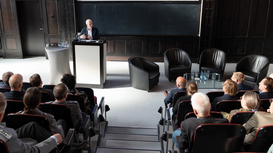 Hamburgs Erster Bürgermeister Dr. Peter Tschentscher Foto des Ersten Bürgermeisters Dr. Peter Tschentscher am Redepult im historischen Hörsaal des BNITM. Im Vordergrun dicht besetzte Sitzreihen.