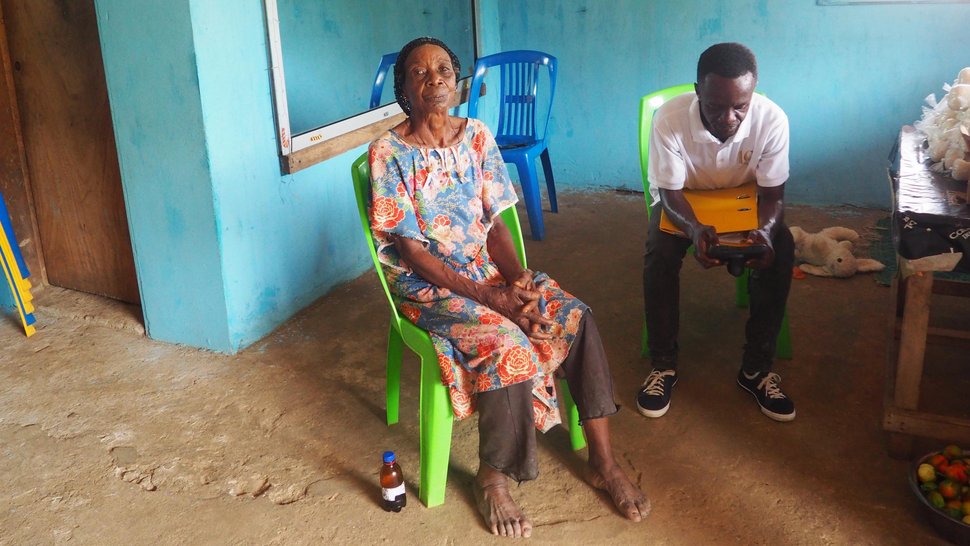 In the waiting room An elderly barefoot woman and a younger man are sitting in a waiting room with mint-coloured walls in Gabon, waiting on bright green plastic chairs.