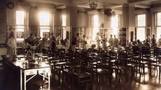 Historical picture in sepia colours of a medical lecture hall with tables and experimental equipment at the seats