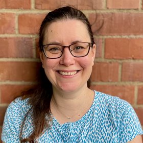 Morlin Milewski Morlin Milewski: A technical assistant laughs into the camera. She wears square glasses, her long brown hair tied in a braid and a blue and white blouse.