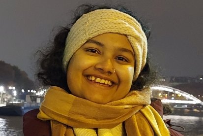 Eine junge Frau lehnt an einer Brücke und lächelt in die Kamera