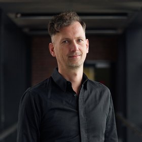 Dr. Ralf Krumkamp Dr. Ralf Krumkamp: ein Forscher mit kurzen, braun-grauen Haaren, trägt ein schwarzes langes Hemd und eine Jeans.