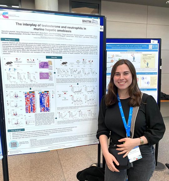Barbara Honecker from RG Lotter stands in front of her poster at the conference, smiles into the camera and waits for interested visitors