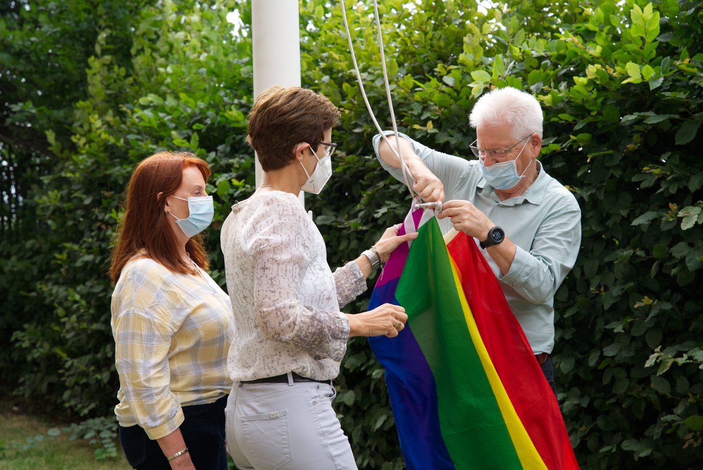 Das Bild zeigt drei Personen beim Hissen der Regenbogeflagge.