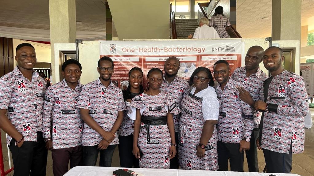 a Ghanaian group of young researchers looking in the direction of the camera and standing in front of a scientific poster