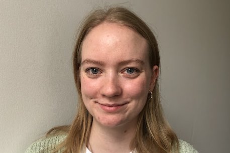 Eine nette junge Frau mit schulterlangem blonden Haar lächelt in die Kamera