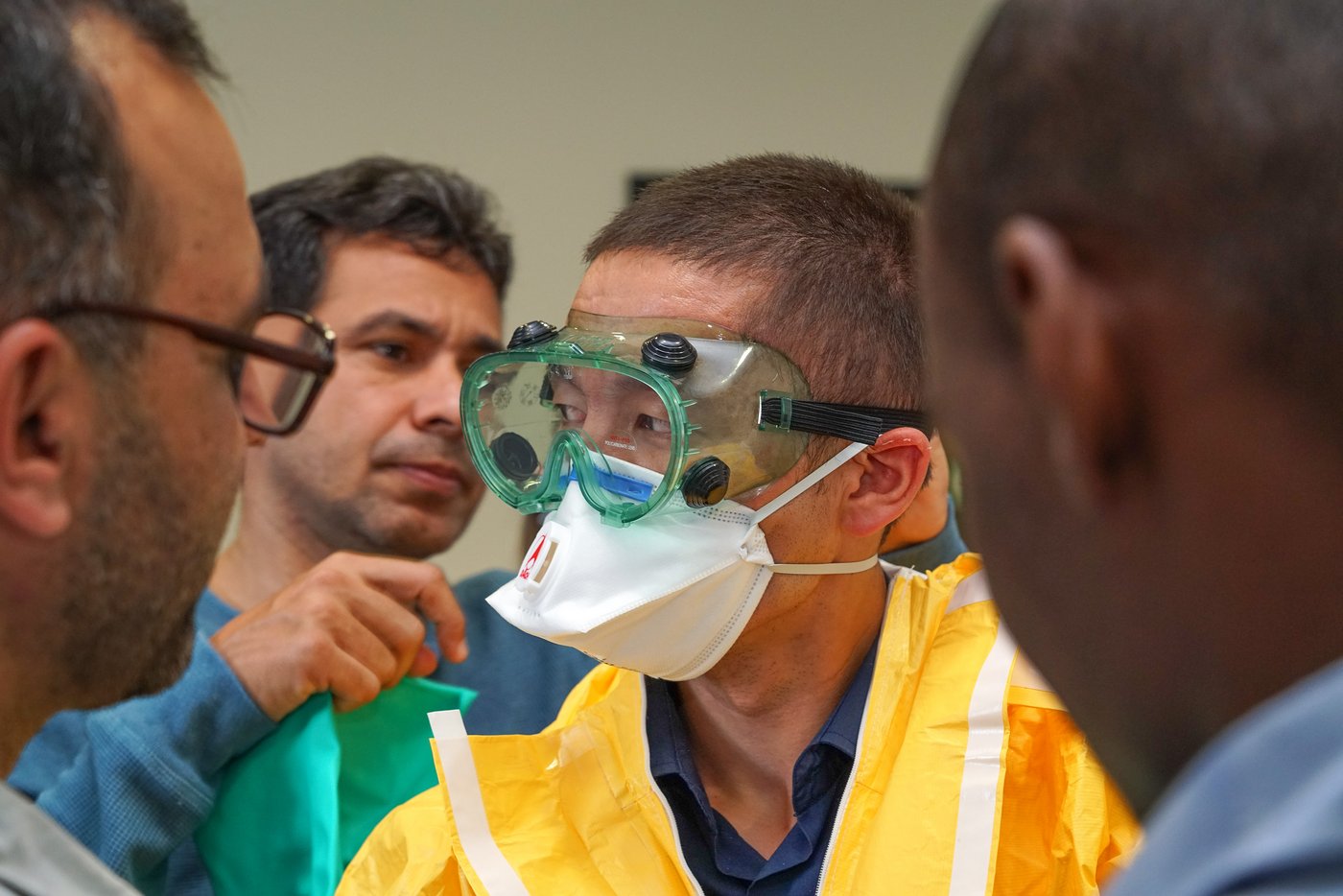 The picture shows several men helping a colleague dress in a personal protective equipment (PPE).