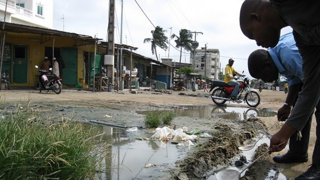 Zwei junge Afrikaner die mit einer Kelle etwas Wasser aus einem Rinnsal vom Wegensrand schöpfen