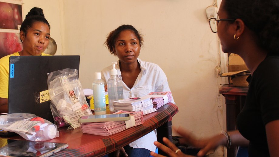 Auf dem Foto sind drei Frauen zu sehen, die um einen Tisch herum sitzen und miteinander reden.