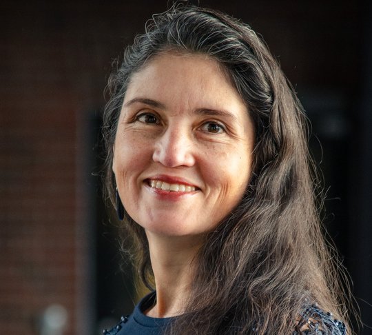 Das Foto zeigt Dr. Andrea Molina Alvarado, eine Forscherin mit langen dunklen Haaren und dunkelblauem Pullover. Sie schaut freundlich in die Kamera.