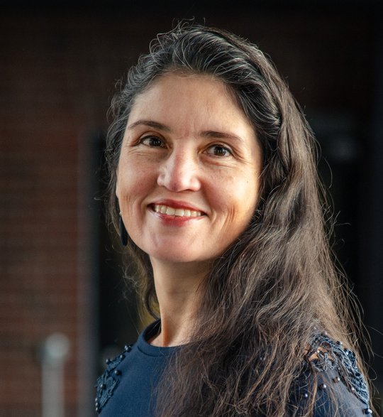 Das Foto zeigt Dr. Andrea Molina Alvarado, eine Forscherin mit langen dunklen Haaren und dunkelblauem Pullover. Sie schaut freundlich in die Kamera.