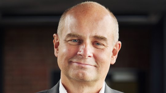 Prof. Dr. Jürgen May:ein Forscher, der eine Glatze hat und ein weißes Hemd mit grauem Sakko trägt.